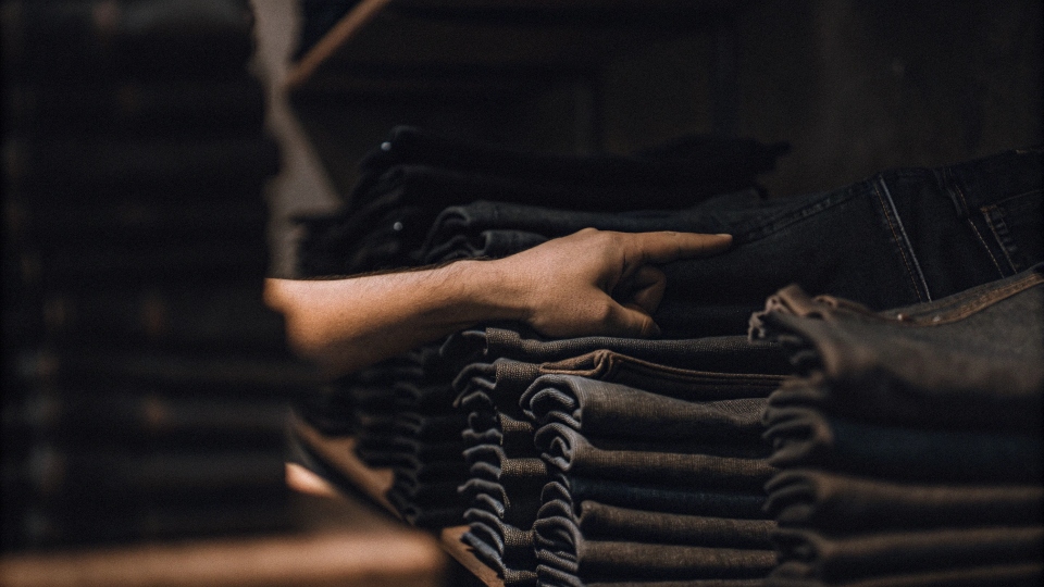 A person pointing to a stack of folded jeans and calling them "denims"