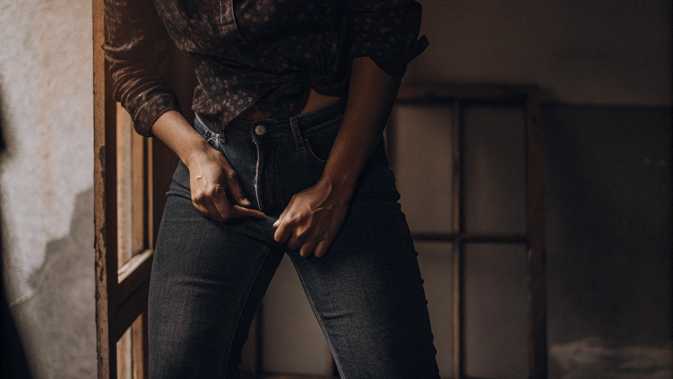 A person looking uncomfortable and adjusting their low-rise jeans
