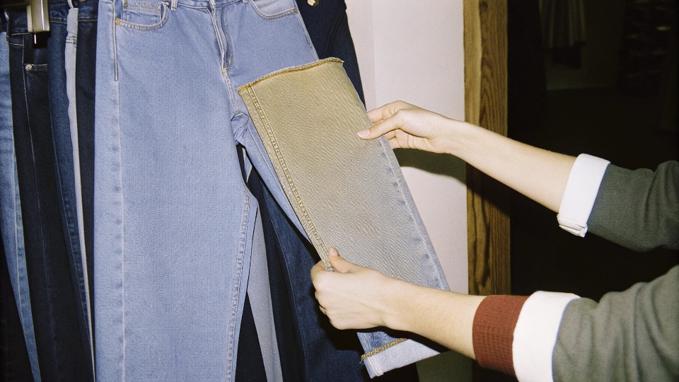Inspecting the Quality of Lightweight Jeans A person inspecting the fabric tag and texture of a pair of jeans in a store