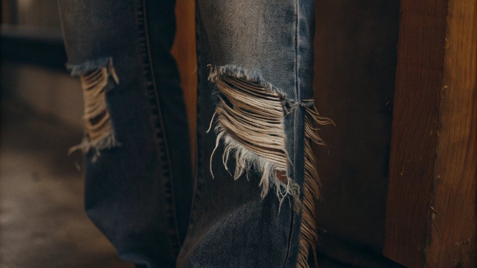 A close-up of a perfectly frayed jean hem, showing the white threads exposed