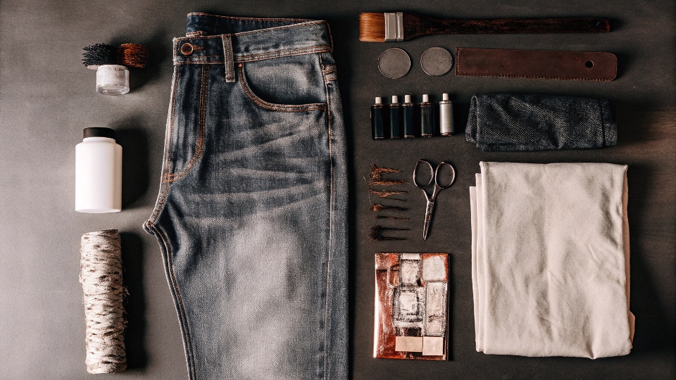 A flat lay of supplies for making senior jeans: paints, brushes, patches, and a pair of jeans
