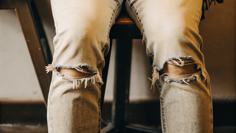 A close-up showing worn-out elastic fibers creating baggy knees on an old pair of stretch jeans