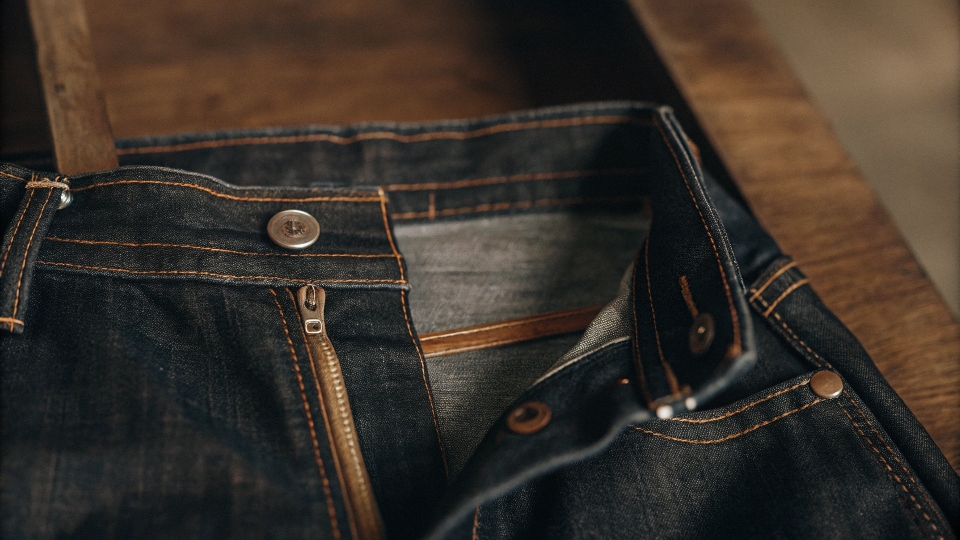 An exploded view diagram showing every component of a pair of jeans, from the fabric down to a single rivet