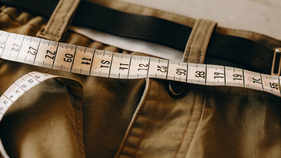 A measuring tape showing the difference between a men's waist measurement and a women's numerical size tag