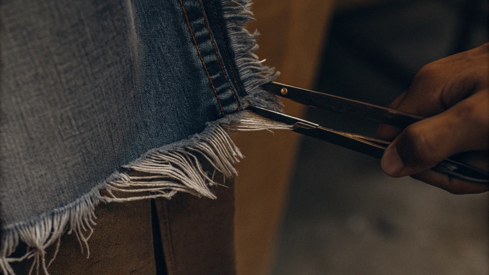 A close-up of a perfectly frayed denim short hem, with tweezers pulling at the threads