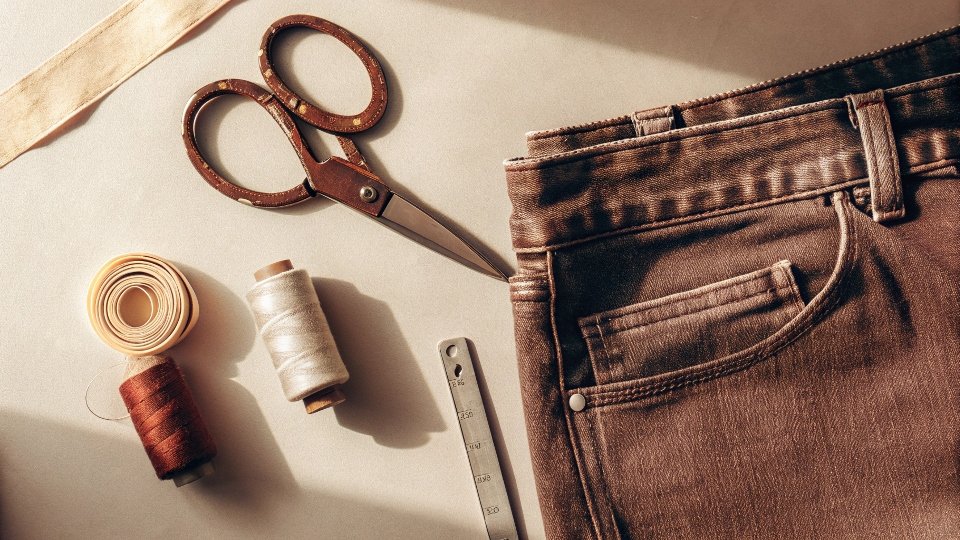 A flat lay of denim fabric, sewing scissors, a tape measure, and thread
