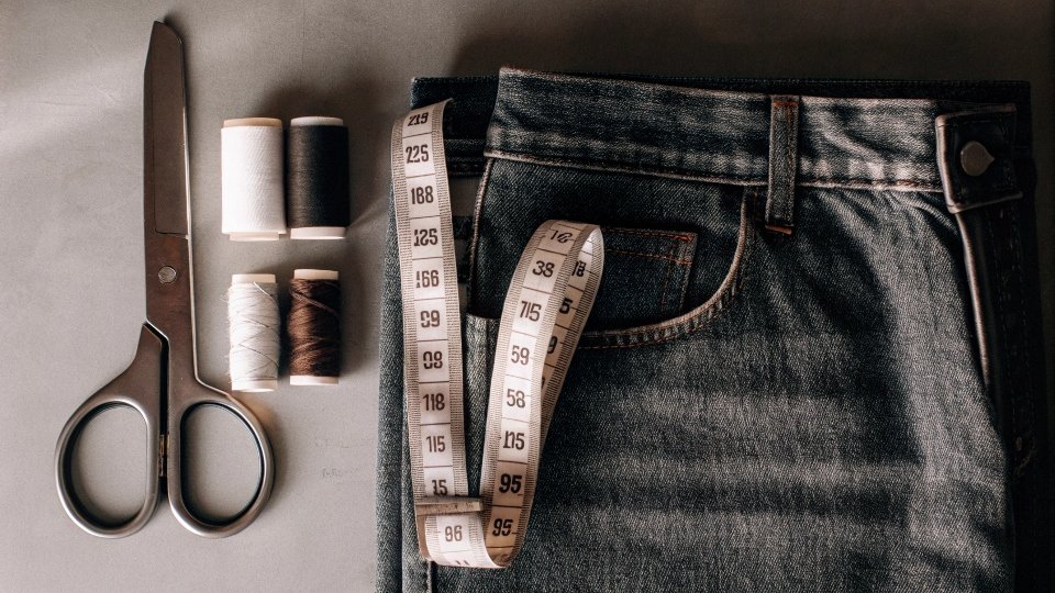 A flat lay of denim fabric, sewing scissors, a tape measure, and thread