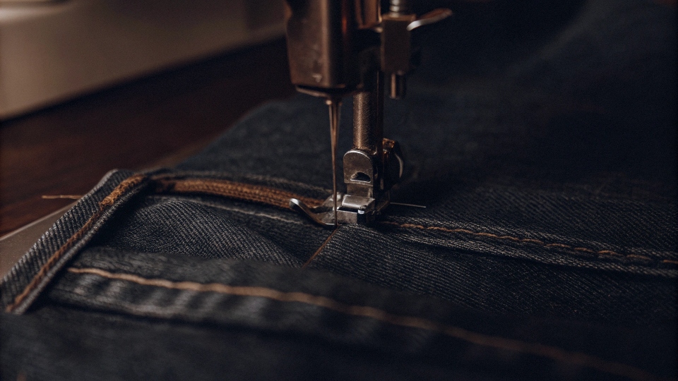 A [sewing machine](https://diznewjeans.com/how-can-you-make-jeans-into-skinny-jeans/)[^6] stitching down the pinned inseam of a pair of blue jeans