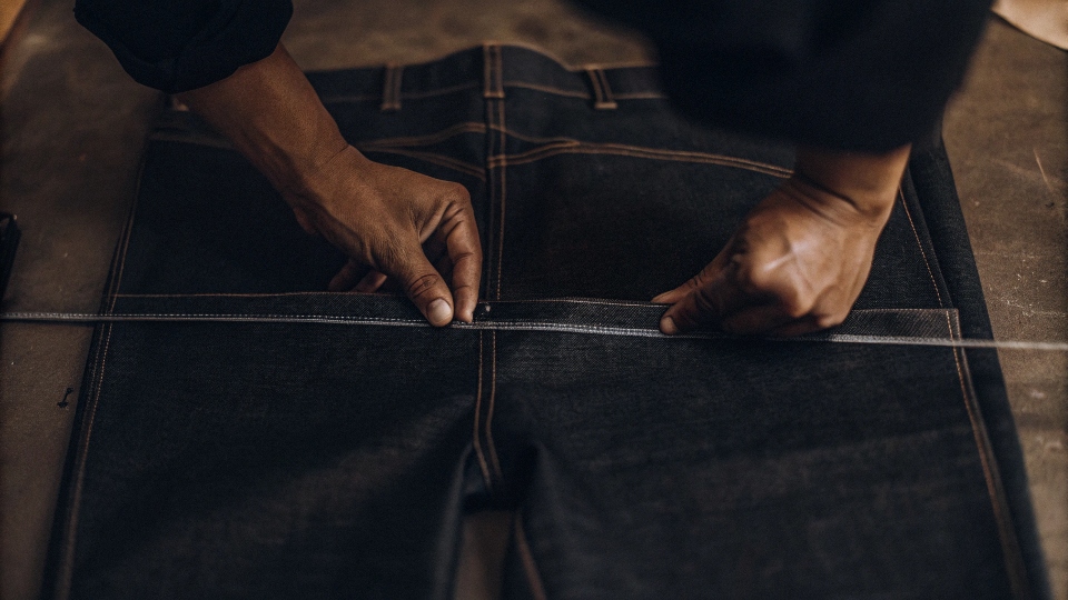 A person using tailor's chalk to draw a tapering line along the calf of a pair of jeans