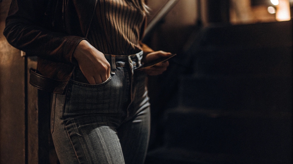 A woman trying to fit her smartphone into the tiny front pocket of her jeans