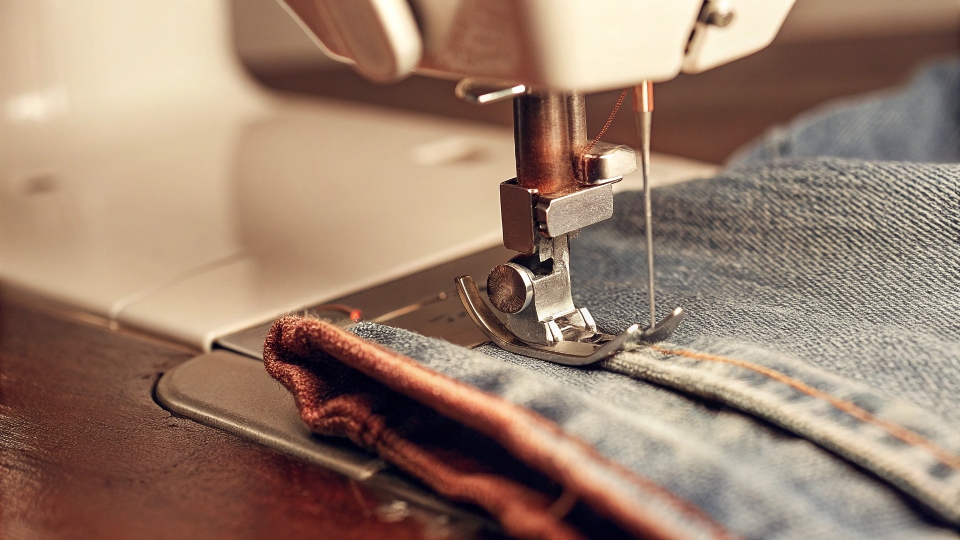 A heavy-duty sewing machine needle stitching through thick blue denim fabric