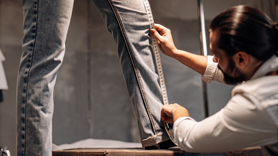 Professional Tailor Altering Jeans A professional tailor carefully measuring the leg opening on a pair of jeans