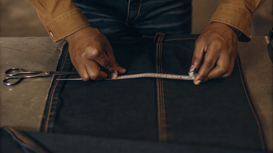 A tailor measuring the inseam of a pair of jeans with a tape measure