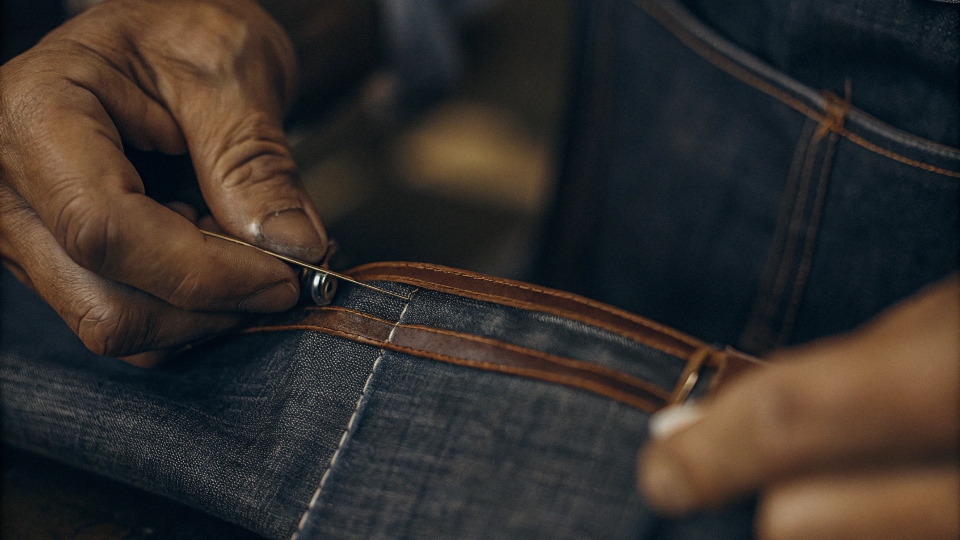 A person's hands carefully [hand-sewing](https://diznewjeans.com/how-do-you-make-a-quilt-out-of-old-jeans/)[^6] a thick denim seam with a needle and thimble