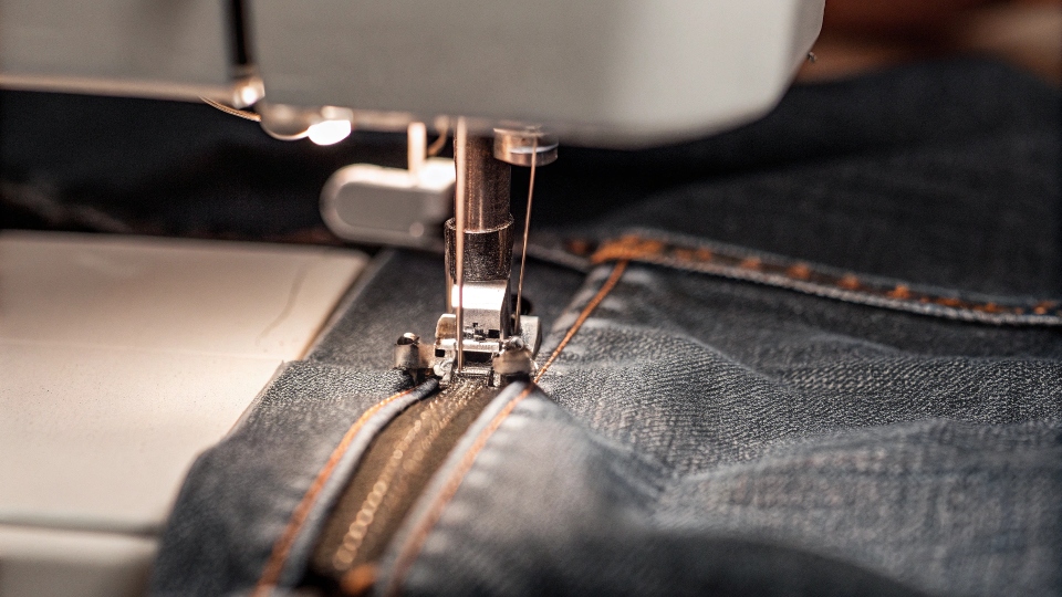 A close-up of a denim gusset being sewn into the outer seam of a pair of jeans