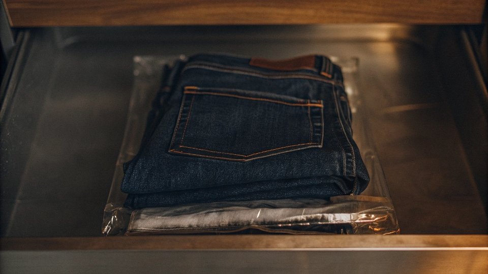 A neatly folded pair of jeans inside a clear, sealed plastic bag, placed in a freezer drawer