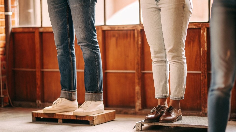 A scale weighing a pair of men's raw denim jeans against a pair of women's stretch jeans