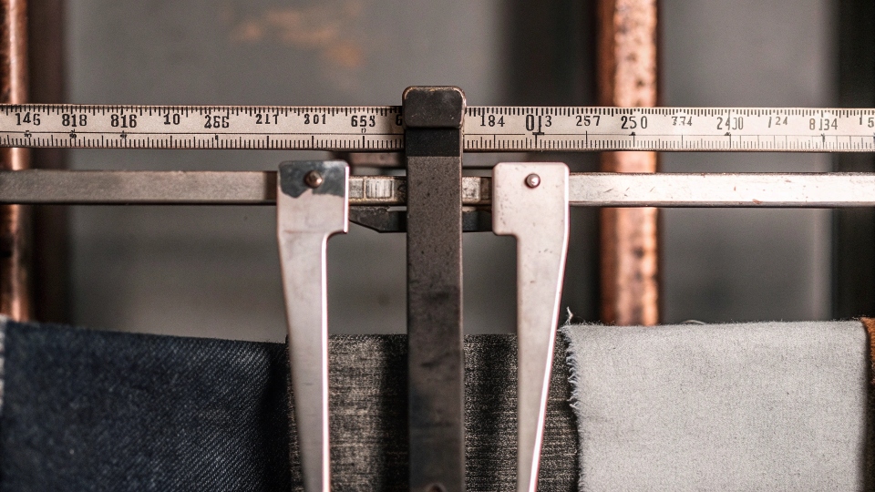 A close-up of a scale weighing a swatch of denim fabric to show its ounce weight