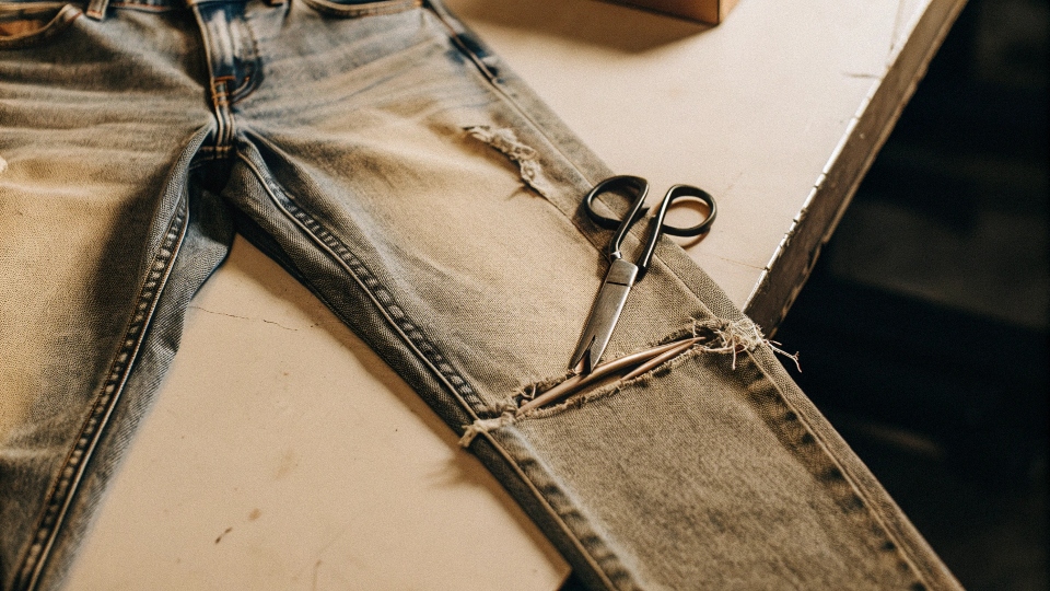 A pair of old jeans with one leg cut off and scissors lying nearby