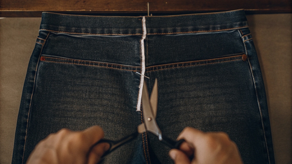 Cutting high-waisted jeans into low-rise Scissors cutting along a chalk line at the top of a pair of high-waisted jeans