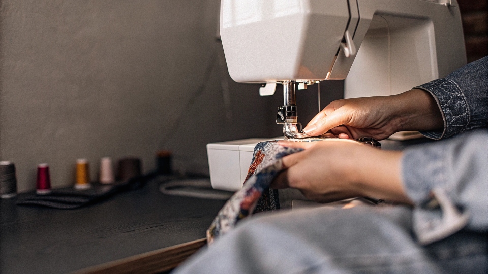 A person at a home [sewing machine](https://diznewjeans.com/how-to-make-your-own-blue-jeans/)[^8] attaching a colorful fabric cuff to a jean leg