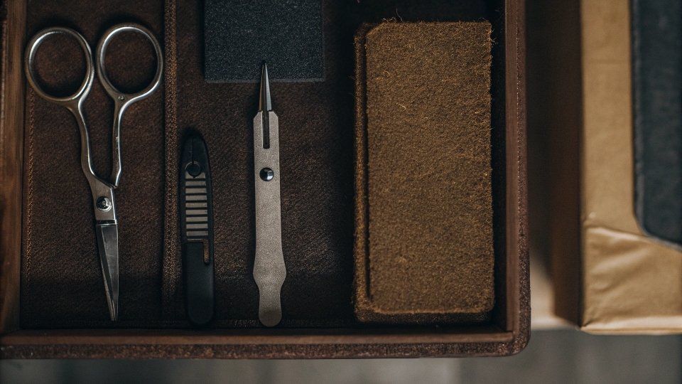 A flat lay of basic tools for distressing jeans: sandpaper, scissors, tweezers, and a box cutter