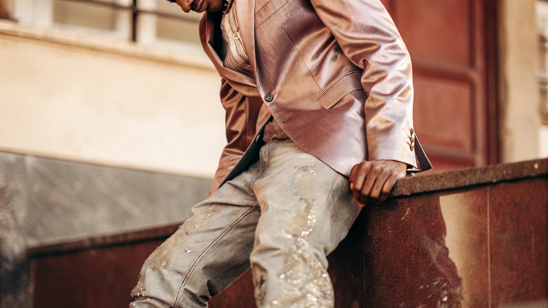 A man awkwardly wearing a formal, shiny suit jacket with faded, casual jeans