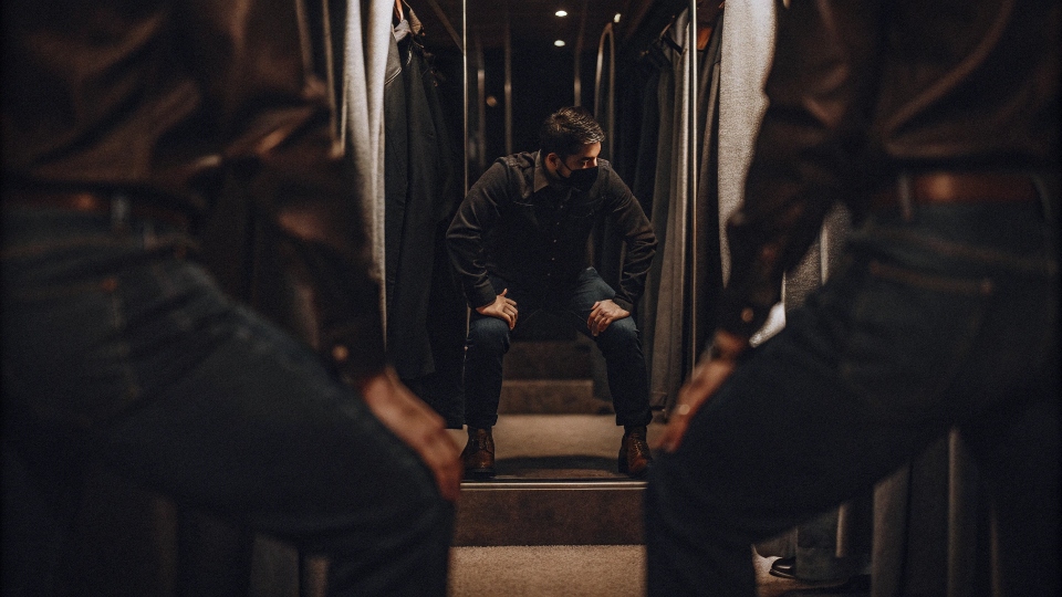 A man in a fitting room doing a squat in a new pair of jeans to test the fit