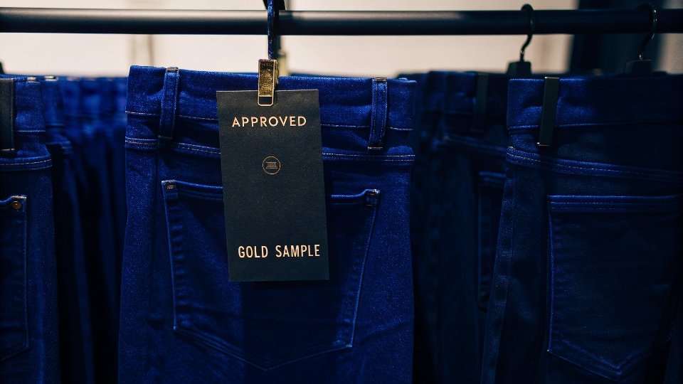The Gold Standard Sample for Jeans Production A final approved "gold sample" pair of jeans with a signed tag hanging from the belt loop.