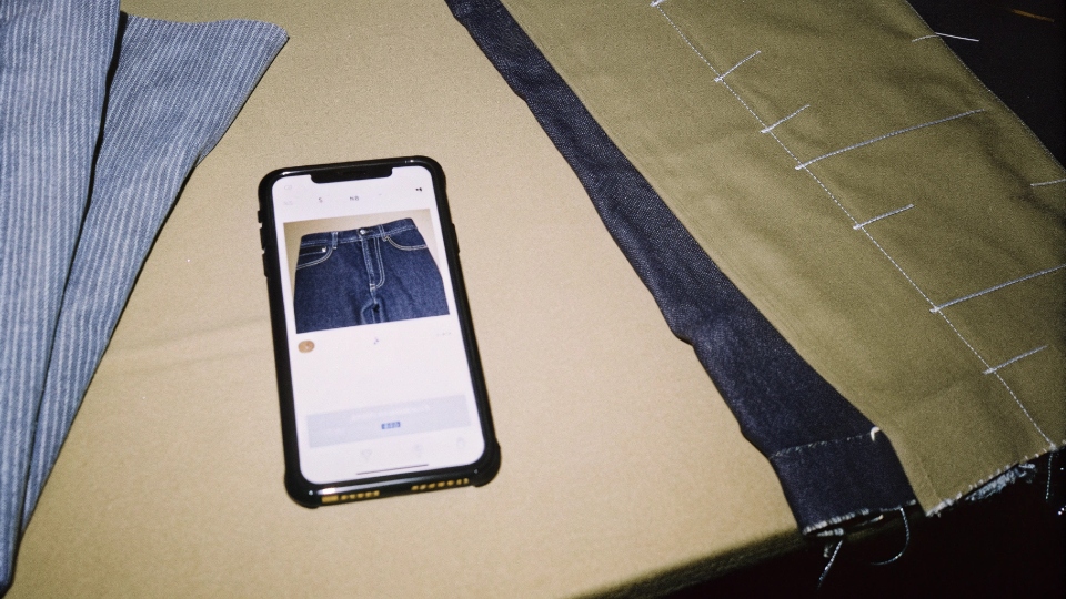 A smartphone showing a photo update from a factory manager of jeans on the sewing line