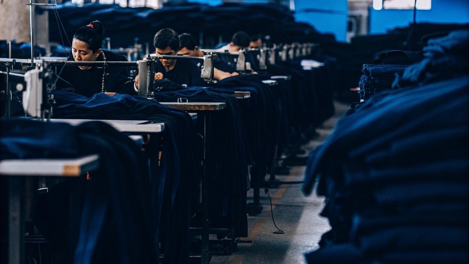 Factory Worker Sewing Daily Output A factory floor with workers at sewing machines in an assembly line.