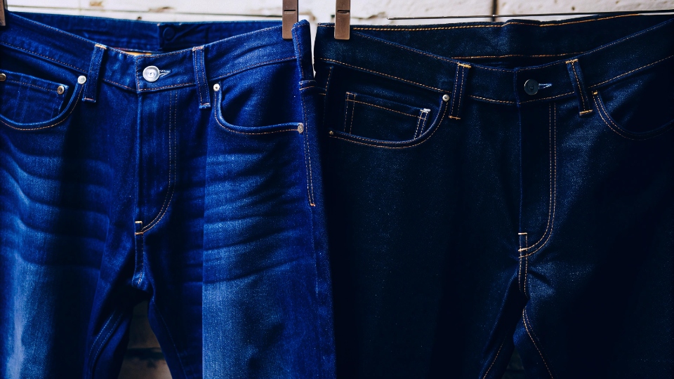 The Lifespan of Quality Denim Jeans A pair of beautifully faded raw denim jeans hanging next to a brand new, dark pair.