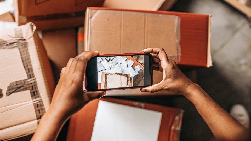 How to File a Claim for Cargo Losses A person taking a photo of a damaged shipping box with a smartphone to document it for an insurance claim.