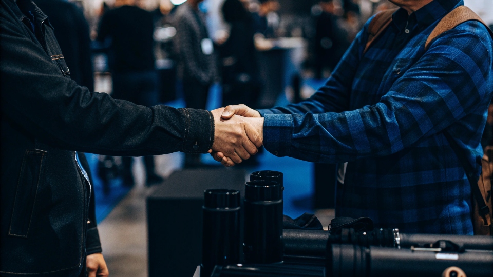 How to Find a Clothing Manufacturer A person attending a trade show, shaking hands with a factory representative at a booth.
