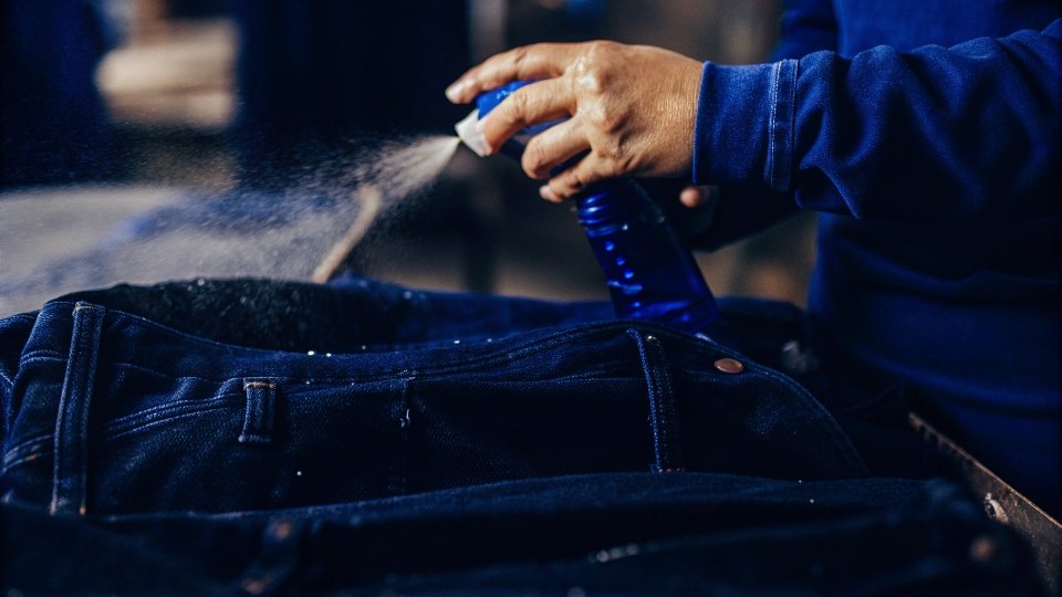 Spot Shrinking Jeans Waistband A person using a spray bottle to dampen the waistband of a pair of jeans.