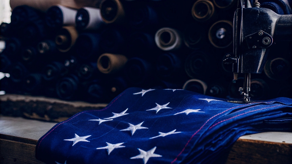Jeans Brands Made in the USA An American flag next to a vintage sewing machine making a pair of denim jeans.