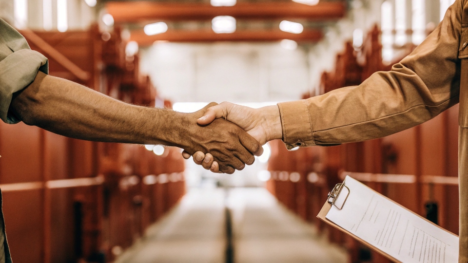 Transparent Factory Subcontracting Policy Agreement A handshake over a signed contract in a factory setting, symbolizing trust and agreement.