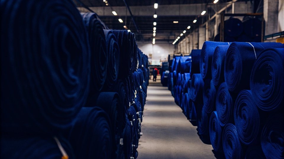 A Global Denim Manufacturing Mill Massive rolls of denim fabric in a large, modern textile mill.