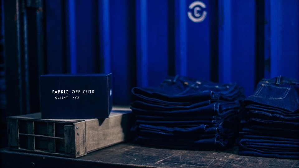 Fabric Off-Cuts Ready for Pickup A carton labeled 'FABRIC OFF-CUTS - CLIENT XYZ' sitting next to cartons of finished jeans ready for shipment.