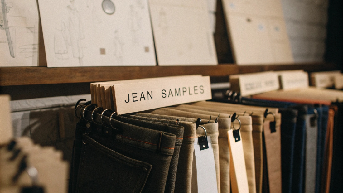 Custom Jean Sample Ownership and Management A collection of jean samples, neatly tagged and organized on a shelf in a design studio.
