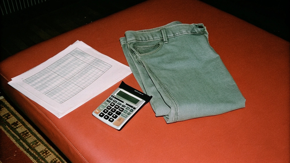 A calculator and a pair of jeans on a shipping manifest, visualizing landed cost calculation