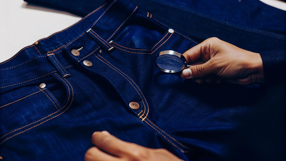 Cost to Manufacture a Pair of Jeans A factory worker's hand holding a price tag for a single pair of jeans, showing cost breakdown.