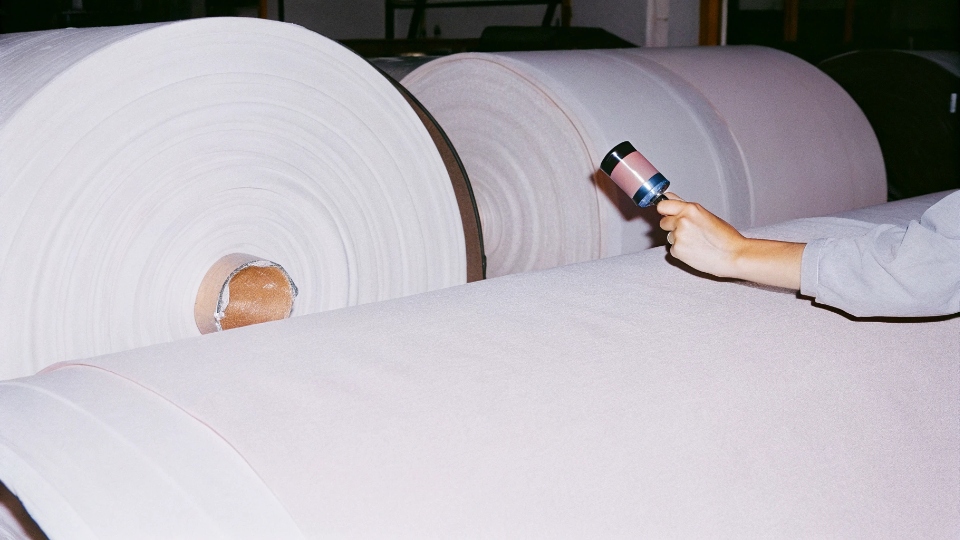 Verifying Denim Fabric Quality and Composition A denim factory worker inspecting a large roll of denim fabric with a magnifying glass