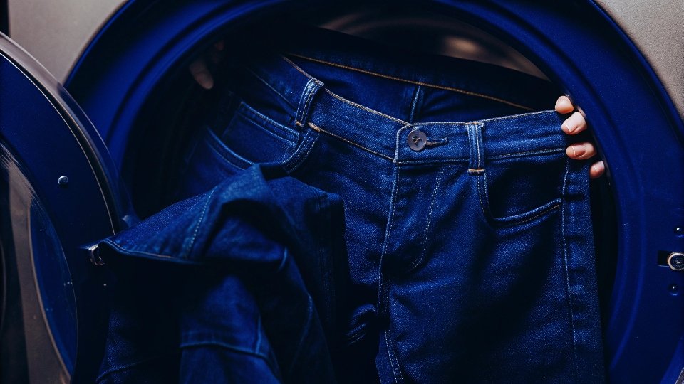 Washing Jeans on a Hot Cycle to Shrink Them A pair of jeans being placed into a high-efficiency front-loading washing machine.