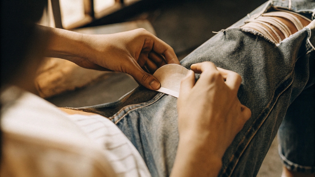 Proactively Patching Jeans A person ironing a denim patch onto the inside of the thigh area of a pair of jeans.