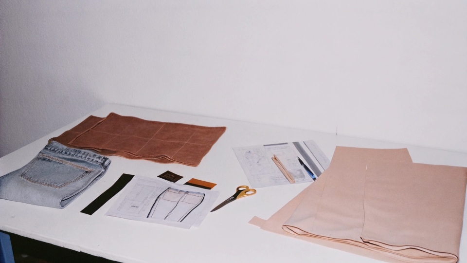 A designer's desk with fabric swatches, sketches, and a sample pair of jeans