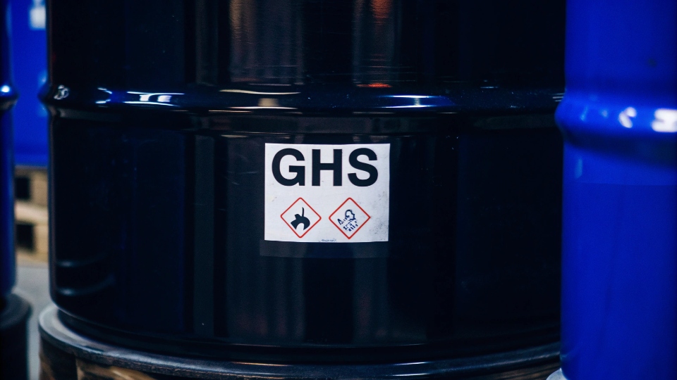 A close-up of a GHS hazard pictogram label on a chemical drum