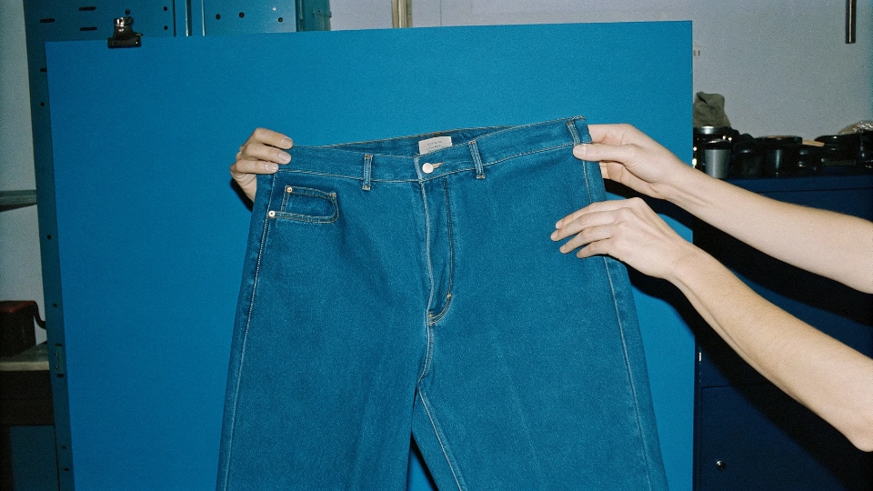 A wash technician comparing a freshly washed pair of jeans to an approved master sample under controlled lighting