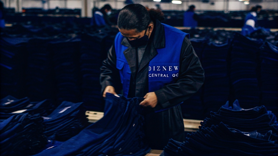 Central Quality Control Team A QC inspector with a "DiZNEW Central QC" vest reviewing a line of jeans at a factory.