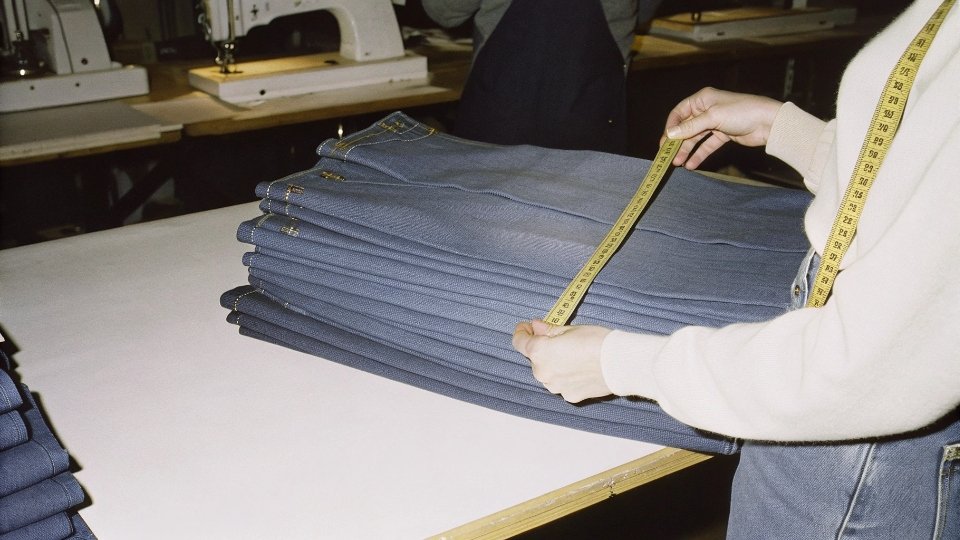 An inspector measuring a stack of cut denim pieces to ensure they match the pattern specifications